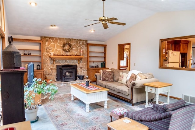 living room with vaulted ceiling, built in features, a wood stove, sink, and ceiling fan