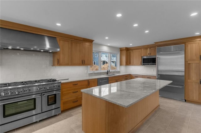 kitchen with appliances with stainless steel finishes, sink, a center island, light stone countertops, and wall chimney exhaust hood