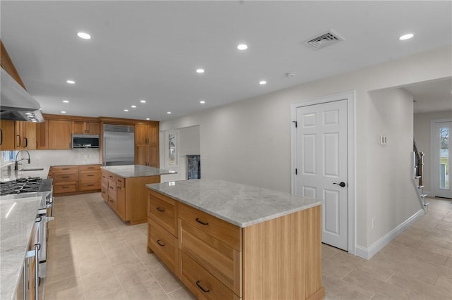 kitchen with stainless steel appliances, light stone countertops, a center island, and sink