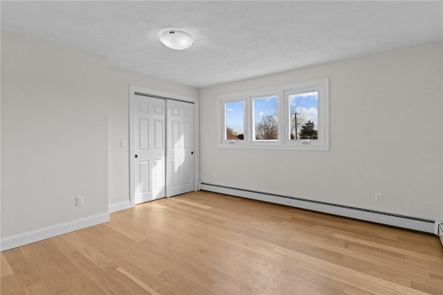 unfurnished bedroom with light hardwood / wood-style floors, a closet, and a baseboard heating unit