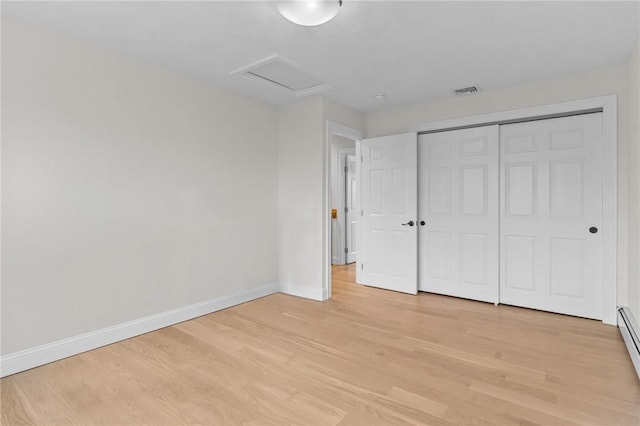 unfurnished bedroom featuring baseboard heating, light hardwood / wood-style floors, and a closet