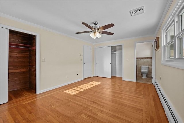 unfurnished bedroom featuring crown molding, ensuite bath, baseboard heating, light hardwood / wood-style floors, and a closet