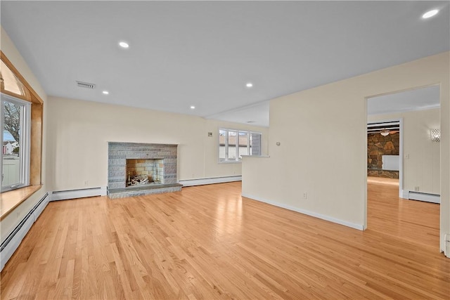 unfurnished living room with a baseboard heating unit, a stone fireplace, and light hardwood / wood-style floors