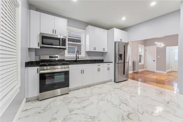 kitchen with radiator, sink, white cabinetry, hanging light fixtures, and stainless steel appliances