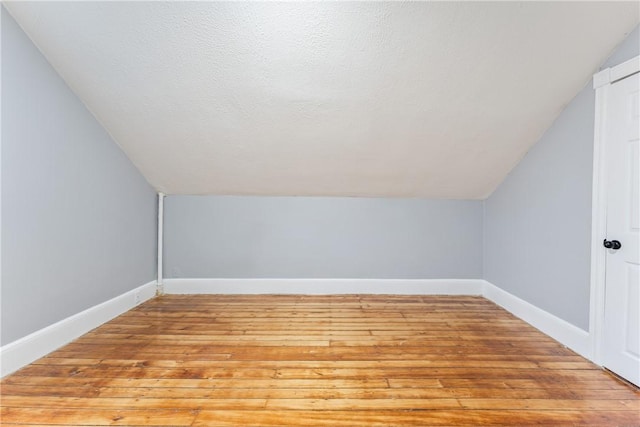 additional living space featuring vaulted ceiling, a textured ceiling, and light wood-type flooring