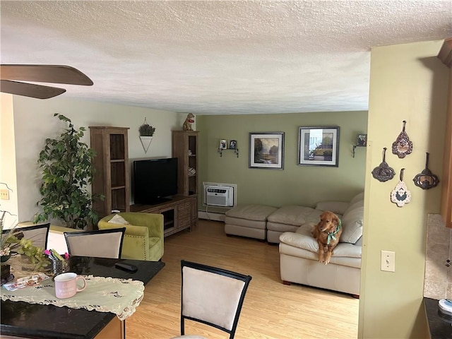 living room featuring baseboard heating, a wall mounted AC, light hardwood / wood-style floors, and a textured ceiling