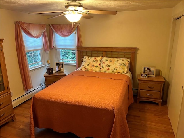 bedroom with a baseboard heating unit, hardwood / wood-style floors, and ceiling fan