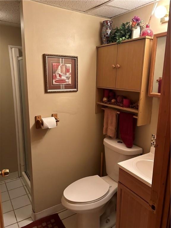 bathroom with a paneled ceiling, tile patterned flooring, vanity, toilet, and walk in shower