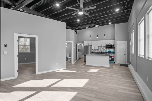 unfurnished living room featuring plenty of natural light, light wood-type flooring, ceiling fan, and a high ceiling