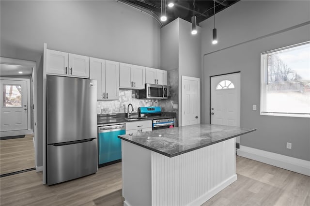 kitchen featuring sink, light hardwood / wood-style flooring, appliances with stainless steel finishes, a towering ceiling, and white cabinets