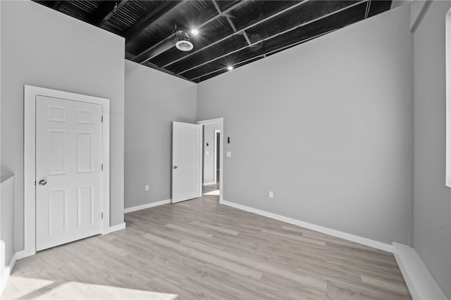 unfurnished room featuring beam ceiling, light hardwood / wood-style flooring, and a high ceiling