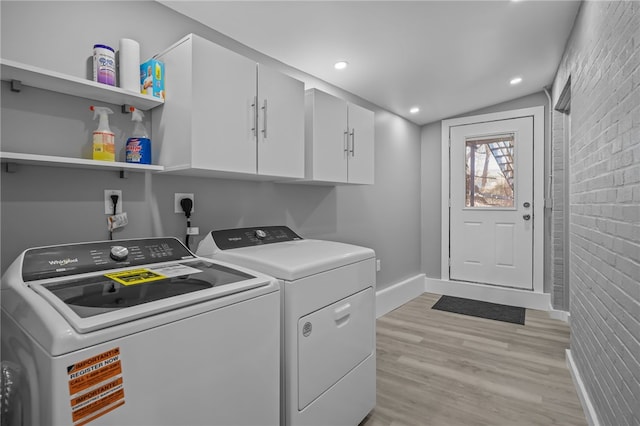 laundry area featuring brick wall, washing machine and dryer, and light hardwood / wood-style flooring