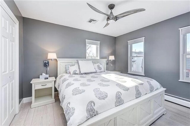 bedroom with a baseboard radiator, light hardwood / wood-style floors, a closet, and ceiling fan