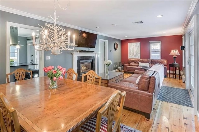 dining room featuring a tiled fireplace, a notable chandelier, ornamental molding, and light wood-type flooring