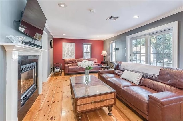 living room featuring crown molding, a premium fireplace, and light wood-type flooring