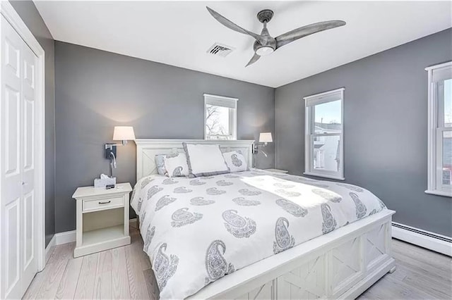 bedroom featuring a baseboard radiator, light hardwood / wood-style floors, a closet, and ceiling fan