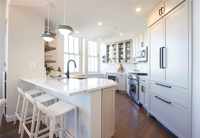 kitchen with a breakfast bar, sink, white cabinetry, appliances with stainless steel finishes, and kitchen peninsula