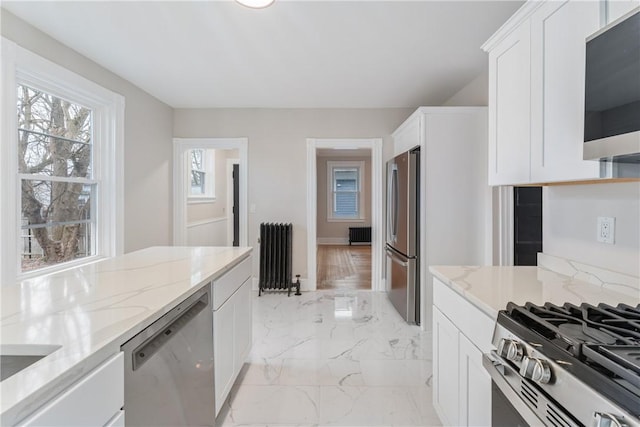 kitchen with white cabinetry, appliances with stainless steel finishes, radiator, and light stone counters