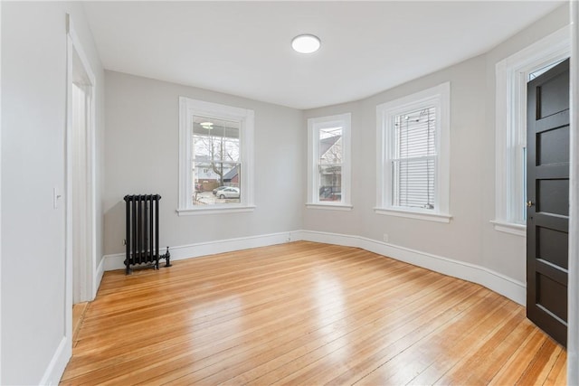 unfurnished room featuring a wealth of natural light, radiator heating unit, and light hardwood / wood-style floors