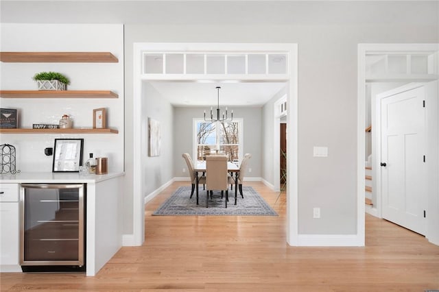 dining area featuring wine cooler, indoor bar, light hardwood / wood-style flooring, and a notable chandelier