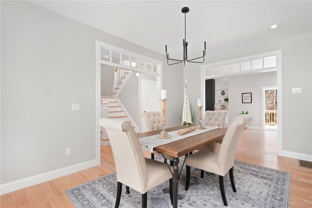 dining area featuring built in features, an inviting chandelier, and light hardwood / wood-style flooring