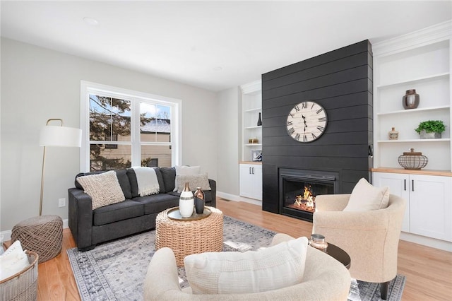 living room with a large fireplace, built in features, and light wood-type flooring