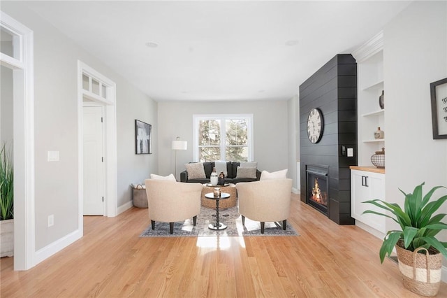 living room featuring light hardwood / wood-style flooring, built in features, and a large fireplace