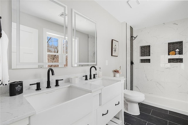 bathroom with tile patterned flooring, vanity, a tile shower, and toilet