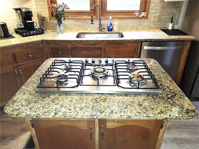 kitchen with sink, backsplash, stainless steel dishwasher, gas cooktop, and light stone counters