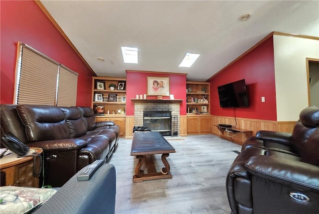 living room with lofted ceiling with skylight, a fireplace, crown molding, and light hardwood / wood-style floors