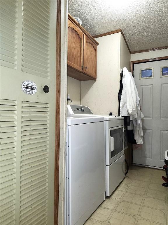 clothes washing area featuring crown molding, cabinets, washing machine and dryer, and a textured ceiling