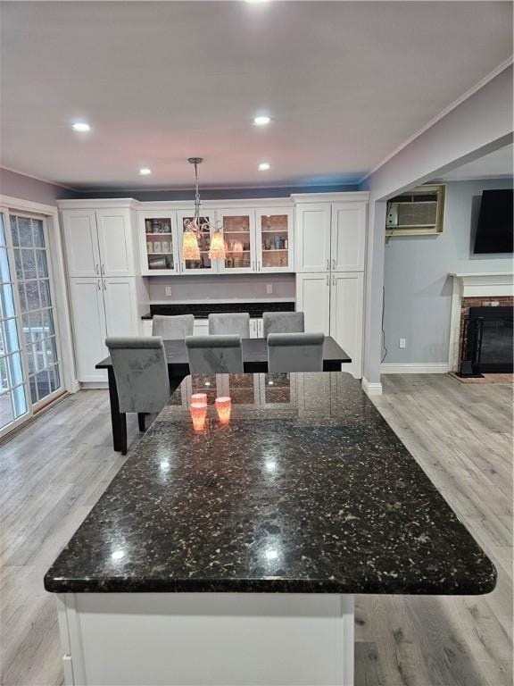 kitchen featuring white cabinetry, a wall mounted air conditioner, dark stone countertops, pendant lighting, and light hardwood / wood-style floors