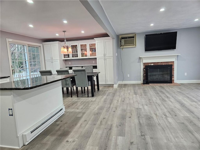 kitchen with a wall mounted AC, dark stone countertops, a baseboard radiator, pendant lighting, and white cabinets