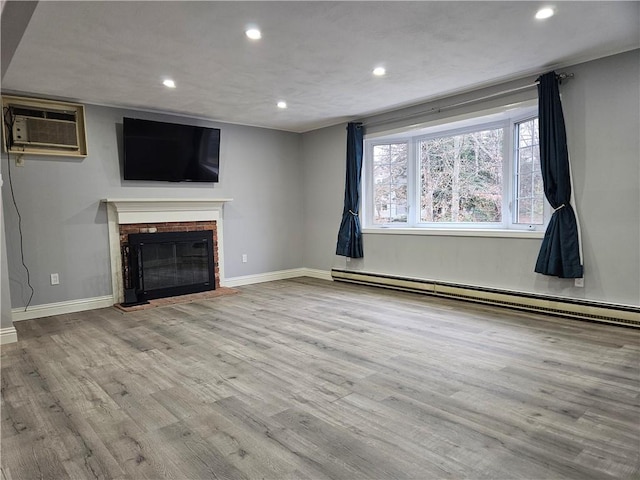 unfurnished living room with a brick fireplace, light wood-type flooring, an AC wall unit, and baseboard heating