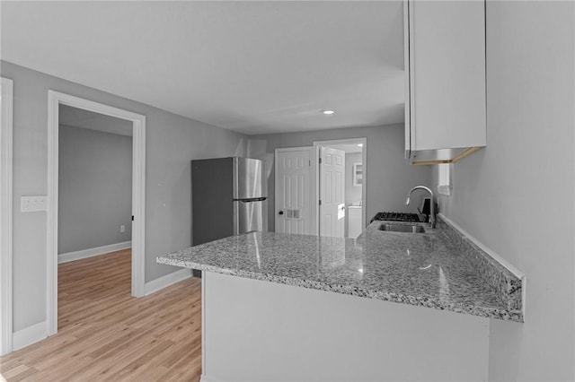 kitchen with sink, stainless steel fridge, light hardwood / wood-style flooring, white cabinetry, and light stone counters