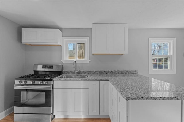 kitchen with sink, plenty of natural light, light stone counters, white cabinets, and stainless steel range with gas cooktop