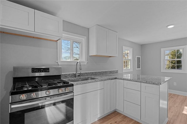 kitchen with white cabinetry, sink, kitchen peninsula, stainless steel gas range oven, and plenty of natural light