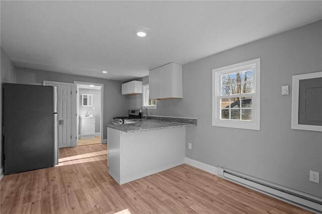 kitchen with a baseboard radiator, appliances with stainless steel finishes, plenty of natural light, kitchen peninsula, and white cabinets