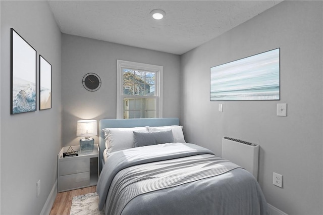 bedroom with radiator, a textured ceiling, and light wood-type flooring