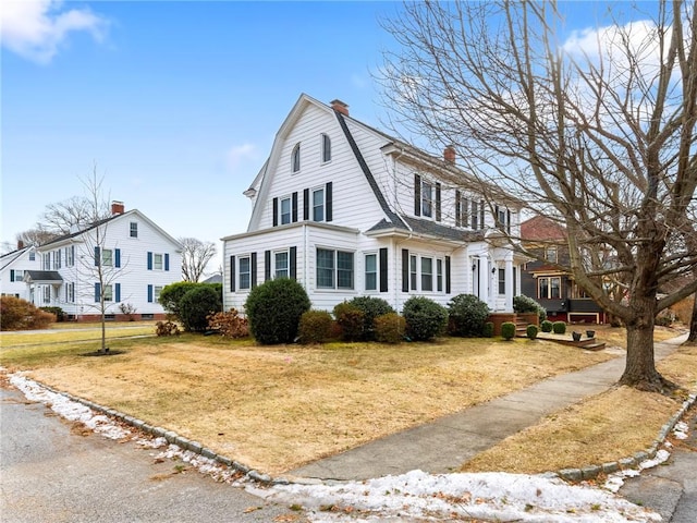 colonial inspired home featuring a chimney, a front yard, and a gambrel roof