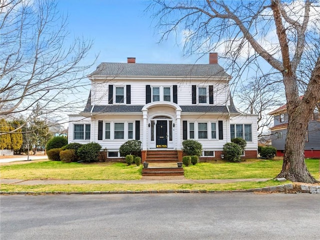 dutch colonial with a shingled roof, a chimney, and a front lawn