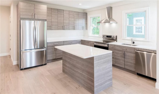 kitchen featuring sink, a center island, light wood-type flooring, stainless steel appliances, and wall chimney range hood