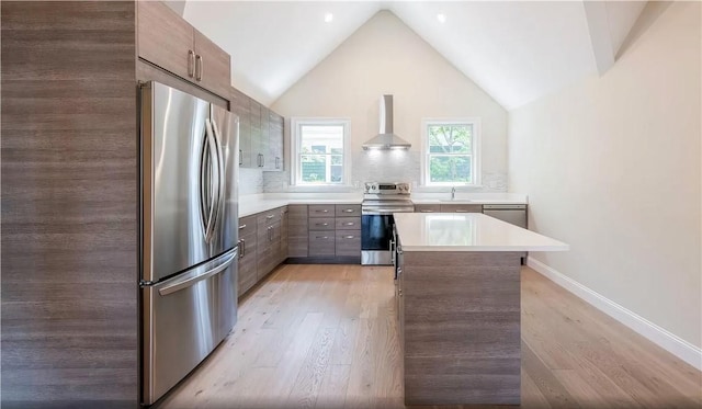 kitchen featuring lofted ceiling, light hardwood / wood-style flooring, appliances with stainless steel finishes, a kitchen island, and wall chimney exhaust hood