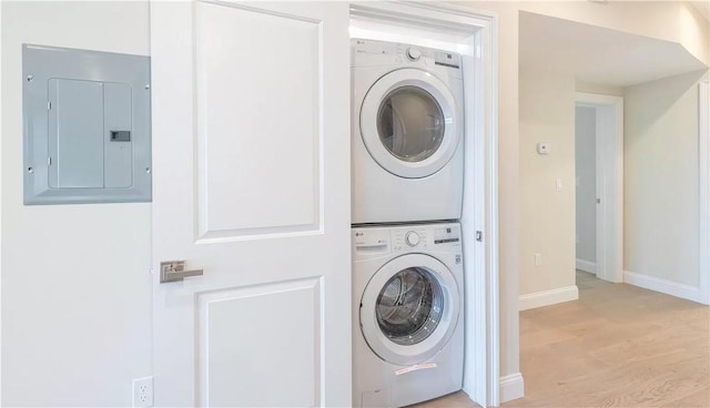 washroom featuring stacked washer and dryer, electric panel, and light wood-type flooring