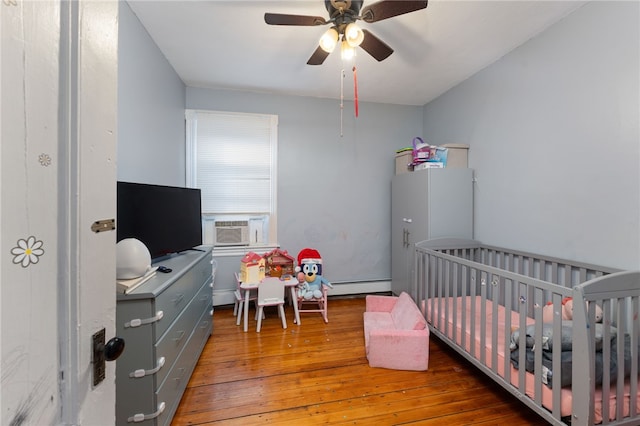 bedroom featuring baseboard heating, ceiling fan, hardwood / wood-style floors, and a crib