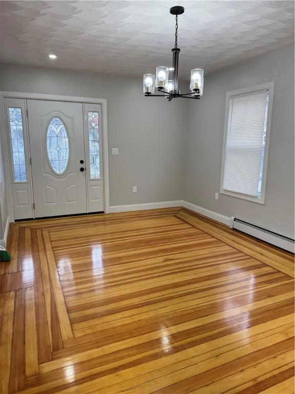 foyer featuring an inviting chandelier, a baseboard heating unit, and light wood-type flooring