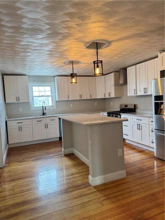 kitchen with white cabinetry, hanging light fixtures, a center island, stainless steel appliances, and wall chimney range hood