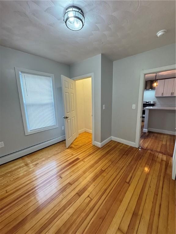 unfurnished room with baseboard heating and light hardwood / wood-style flooring