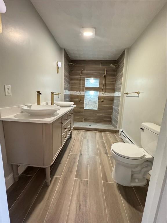 bathroom with a baseboard heating unit, vanity, tiled shower, and toilet