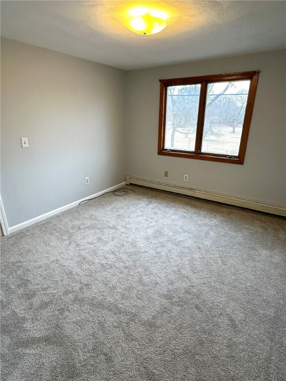 carpeted empty room featuring a baseboard radiator and a textured ceiling